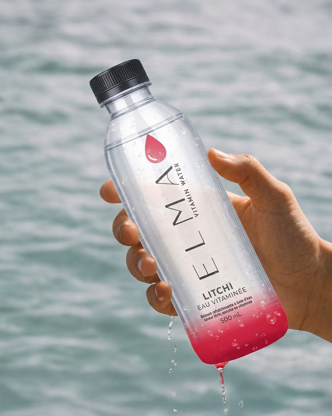 Bouteille ELMA Vitamin Water saveur litchi tenue face à la mer